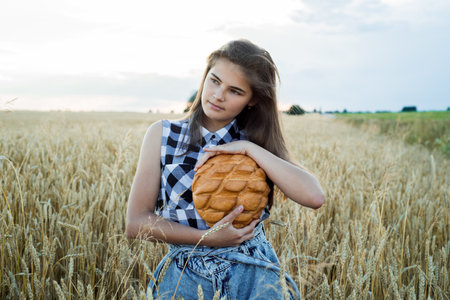 field with ears of corn, harvest of bread.teenager girl holding round bread. Bread Selective focus. Hands holding big bread. Bakery products on a wheat field.の写真素材