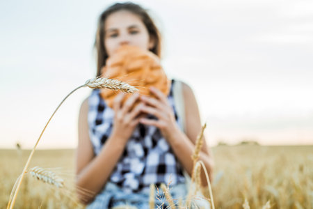 field with ears of corn, harvest of bread.teenager girl holding round bread. Bread Selective focus. Hands holding big bread. Bakery products on a wheat field.の写真素材