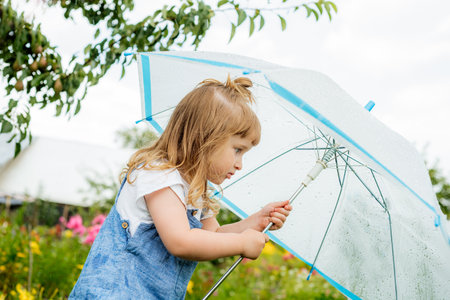 Little girl with umbrella playing in the rain. Autumn outdoor fun for children. Toddler kid outside in the garden. Baby enjoying summer shower.の写真素材
