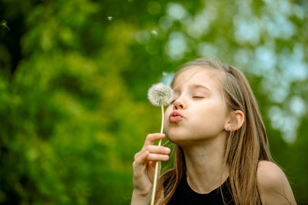 Summer in the park or forest. nature, freshness idea and freedom. happy childhood.Summer joy, little girl blowing dandelion at sunset near the riverの写真素材