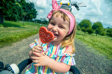 Fashionable baby girl, sunglasses, lollipop like a heart. Happy children hold candy green grass outdoors. Candy shop. Lollipop or sucker on sticks. Sugary treats. Sweet dreamの写真素材