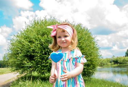 baby girl with lollipop in sunny park. Child Kids play outdoors in summer, eat sweets. Toddler with sweet snack. Kid with unhealthy sugar treat.の写真素材