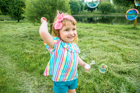 Cute little girl is blowing a soap bubbles.Fashionable baby girl in outdoors park, active games,...