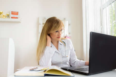 Online doctor consultation at the office. young doctor working on a laptop. speaks and treats distance. conversation with web patient.の写真素材