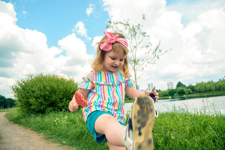 Cute curly baby girl eating watermelon candy in a sunny park. baby with outdoors lollipopの写真素材