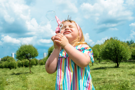 Cute little girl is blowing a soap bubbles.Fashionable baby girl in outdoors park, active games,...