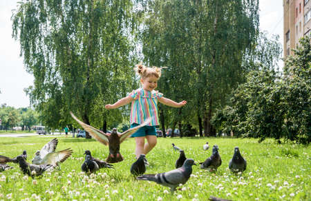 A little girl runs for pigeons.Baby Girl Chasing Pigeons In Outdoors City Park. cheerful happy childhood, runs laughing and screaming.の写真素材