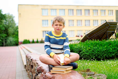 Portrait of Beautiful school boy looking happy outdoors at the day time. Sitting on the steps with books and a large school backpack school theme.の写真素材