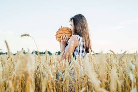 field with ears of corn, harvest of bread.teenager girl holding round bread. Bread Selective focus. Hands holding big bread. Bakery products on a wheat field.の写真素材