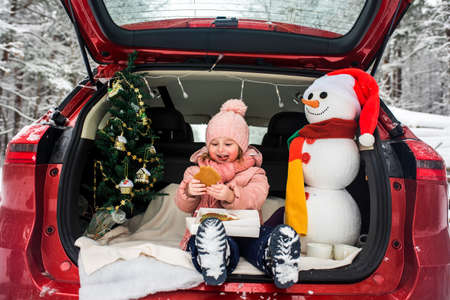 children in the trunk of a car in winter, christmas tree and snowman, merry holidays, hot tea and gingerbread, picnic in the forestの写真素材