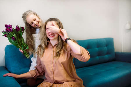 Cute little girl greeting her mother at home. Bouquet of purple tulips. Mothers day conceptの写真素材