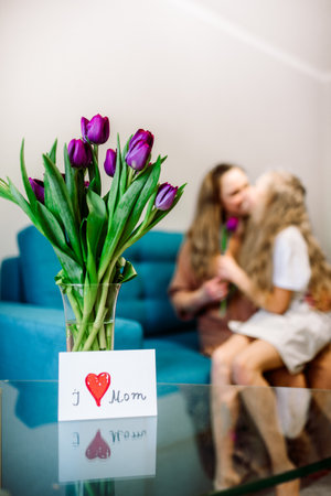 Cute little girl greeting her mother at home. Bouquet of purple tulips. Mothers day conceptの写真素材