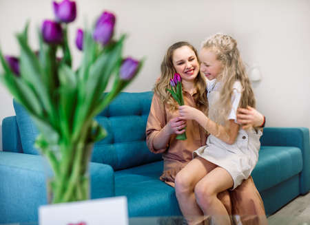 Cute little girl greeting her mother at home. Bouquet of purple tulips. Mothers day conceptの写真素材