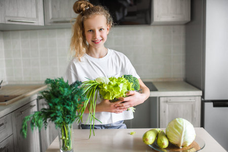 Portrait of cute little girl in the kitchen with green cabbage and broccoli, fresh vegetables and saladの写真素材