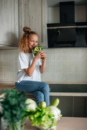 Portrait of cute little girl in the kitchen with green cabbage and broccoli, fresh vegetables and saladの写真素材
