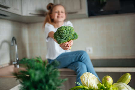 Portrait of cute little girl in the kitchen with green cabbage and broccoli, fresh vegetables and saladの写真素材