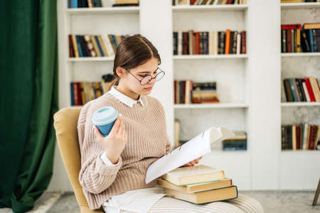 Young girl standing near bookshelf in libraryの写真素材