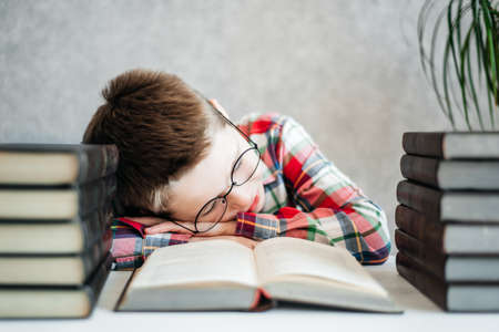 Funny boy with glasses, fell asleep on a book in the library. School and education conceptの写真素材