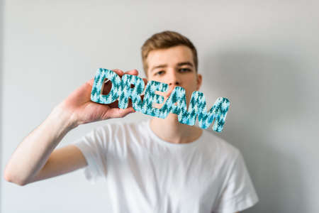 a smiling dreaming guy, young man laying on the blue couch at home. in the hands of the inscription the word dreamの写真素材
