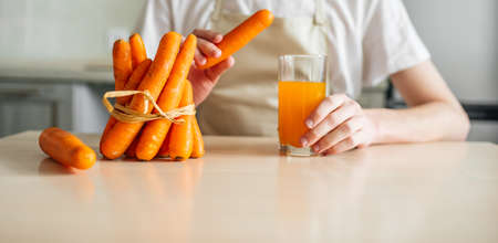 carrots and carrot juice in a glass beaker in the kitchen. Young guy and healthy foodの写真素材
