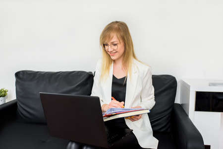 Remote work.Entrepreneur woman wearing white jacket working with a laptop sitting on couch at home.Online consultation of a tax lawyer, accountant in the officeの写真素材