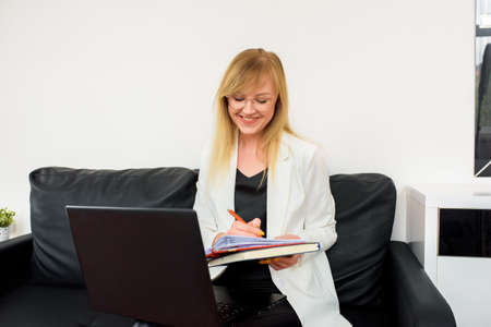 Remote work.Entrepreneur woman wearing white jacket working with a laptop sitting on couch at home.Online consultation of a tax lawyer, accountant in the officeの写真素材