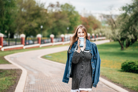 Girl holding coffee and phone, walking on the street to work. Young female worker lifestyle.の写真素材