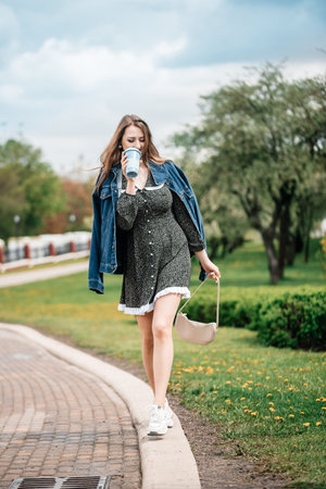 Girl holding coffee and phone, walking on the street to work. Young female worker lifestyle.の写真素材
