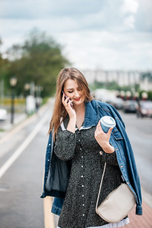 Girl holding coffee and phone, walking on the street to work. Young female worker lifestyle.の写真素材