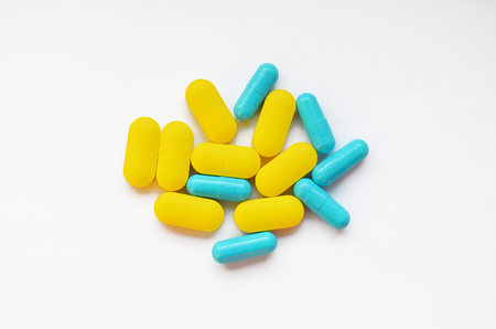 Yellow oval pills and blue capsules on white background, top viewの写真素材