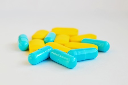 Yellow oval pills and blue capsules on white background, side viewの写真素材
