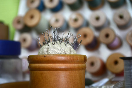 Pins with a round hat in a wooden round box on the background of different color threads
