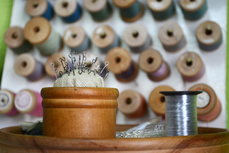 Pins with a round hat in a wooden round box and coil of metal threads on the background of different threadsの写真素材