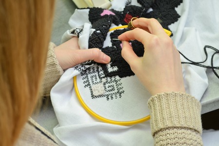 The woman embroiders by hand Ukrainian embroidery on white fabric with black and pink wool threads in the hoop, closeupの写真素材