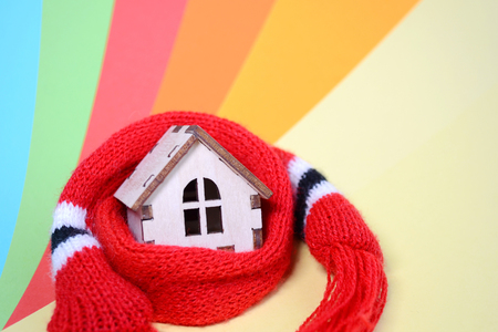 Wooden toy house with windows in a red scarf on a rainbow colored background, warm house, insulation of houses, copyspace, closeupの写真素材