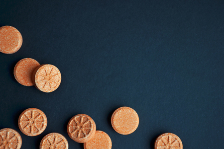 Orange round orange shaped tablets are scattered chaotically on a corner of black background with copyspace.の写真素材