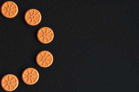 Orange round tablets in the form of an orange lie in the form of a semicircle on a black background with space for textの写真素材