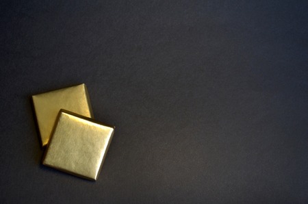 Two square pieces of chocolate with Golden foil on a black background with space for text.の写真素材