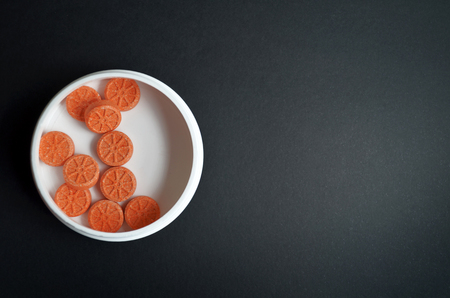 Orange round pills in the shape of an orange lie in a round white jar on a gray background with copyspace.の写真素材