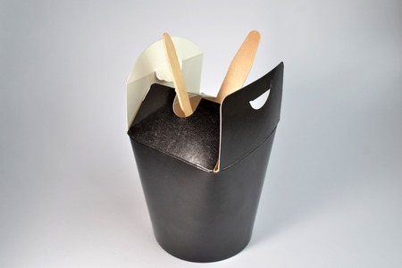 Disposable black square cardboard takeaway food open container on white background, inside of them is wooden spoon and forkの写真素材
