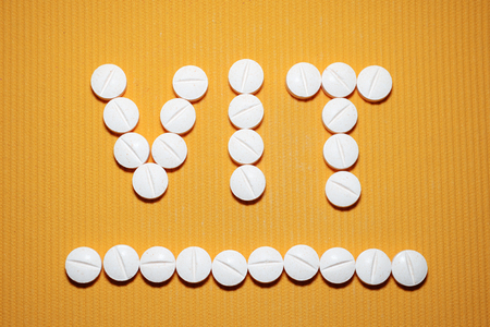 Lots of white smooth convex tablets with dividing strip on yellow striped background, in form of word VIT, underlined, vitamins, top viewの写真素材