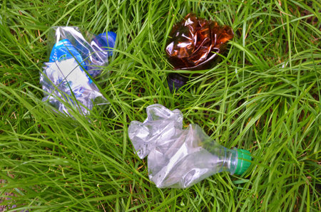 Crumpled white and brown plastic bottles lie on the grass, garbage in grass closeup