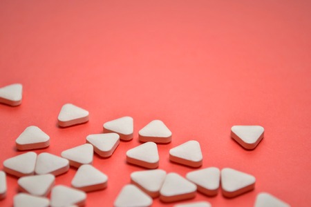 White triangular unusual pills scattered on a coral background with copyspaceの写真素材