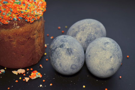 Easter cake with powder, with eggs colored by hibiskus tea on a black background in a beam of light,...