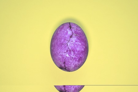 Purple egg with crack, painted in tea hibiscus, on a yellow background, similar to dragon eggs and marble with copyspaceの写真素材