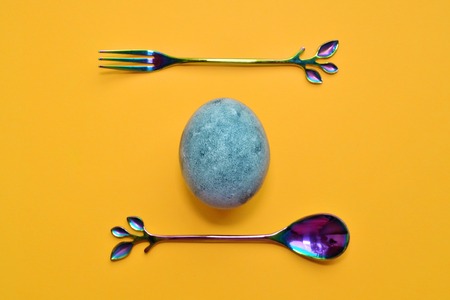 Blue egg with rainbow fork and spoon, painted in tea hibiscus, on orange background, similar to dragon eggs and marble with copyspaceの写真素材