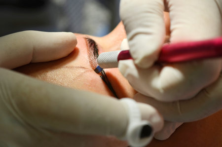 Girl lying on procedure of microblading. Cosmetologist in white gloves makes permanent makeup on...
