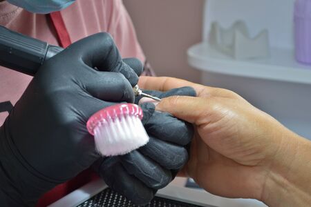 Manicurist in black gloves and with brush makes hardware manicure by fine cutterの写真素材