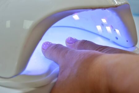 Pink gel polish fingers dries in the ultraviolet lamp, closeupの写真素材