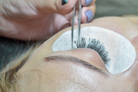 The extension of artificial eyelashes on an adult woman, the master spreads the eyelashes with tweezer, top viewの写真素材